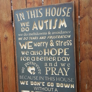 May include: A wooden sign with a blue background and gold lettering. The sign reads "In this house we do autism. We do meltdowns & avoidance. We do tears and frustration. We worry & stress. We also hope for a better day and we persevere and we pray. Because in this house we don't go down without a fight!"