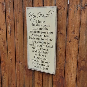 Può includere: Un cartello di legno bianco con testo nero che recita "My Wish Spero che i giorni arrivino facili e che i momenti passino lentamente E ogni strada ti porta dove vuoi andare E se ti trovi di fronte a una scelta, e devi scegliere Spero che tu scelga quello che conta di più per te"