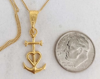 May include: A gold chain necklace with a pendant featuring a heart, cross, and anchor design. The pendant is about the size of a UK ten pence coin.