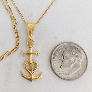 May include: A gold chain necklace with a pendant featuring a heart, cross, and anchor design. The pendant is about the size of a US dime.
