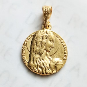 May include: Gold-toned pendant featuring a relief of Mary Magdalene with the inscription "Sancta Maria Magdalena".