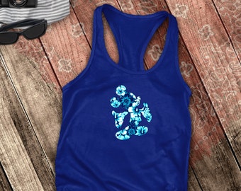 May include: A royal blue tank top with a floral Mickey Mouse design in shades of blue and white. The tank top is a racerback style and is laying on a wooden surface. Sunglasses, a camera, and flip-flops are also visible.