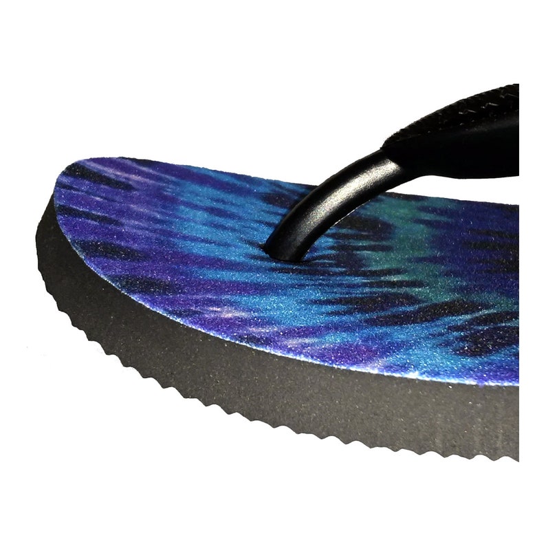 May include: Close-up of a blue and purple tie-dye flip-flop with a black strap. The sole has a textured edge.