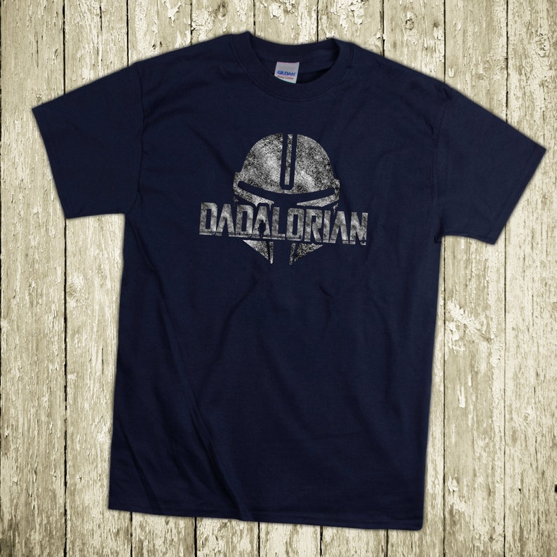 Puede incluir: Camiseta azul marino con un gr&aacute;fico blanco desgastado de un casco y la palabra "DADALORIAN". La camiseta est&aacute; hecha de un material suave y es adecuada para uso casual. El dise&ntilde;o es un juego de palabras con "Mandalorian".