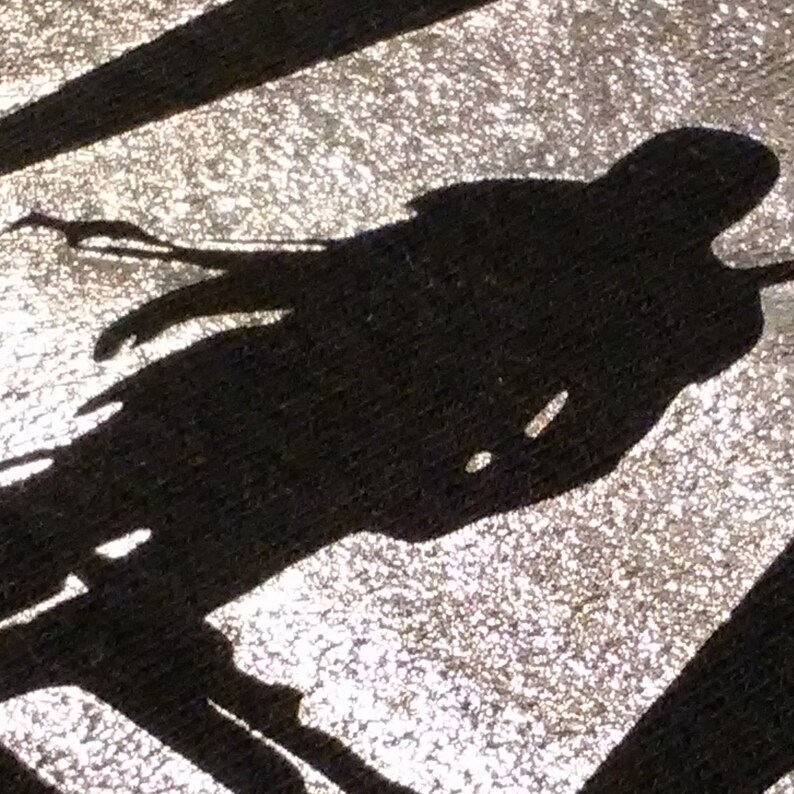 Puede incluir: Silueta negra de una persona en movimiento, posiblemente corriendo o patinando, sobre un fondo plateado texturizado. La imagen tiene una calidad gr&aacute;fica de alto contraste, con l&iacute;neas n&iacute;tidas y una sensaci&oacute;n din&aacute;mica.