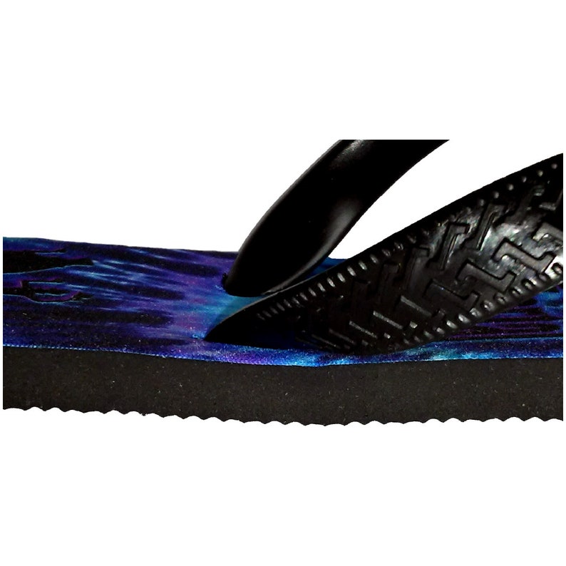 May include: Close-up of a black flip-flop with a blue and purple tie-dye pattern on the footbed. The flip-flop has a textured black strap and a black sole.