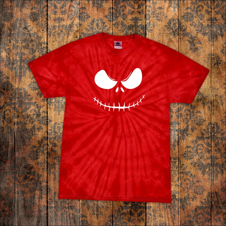 May include: Red tie-dye t-shirt featuring a white, stylized face with large eyes and a stitched-mouth design. The shirt is a classic crew neck style, perfect for Halloween or costume parties. The design is centered on the front of the shirt.