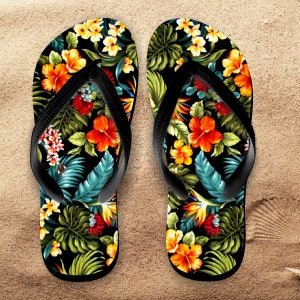 May include: Pair of black flip-flops with a tropical floral print featuring hibiscus flowers, palm leaves, and birds of paradise. The flowers are in shades of orange, yellow, and red.