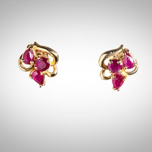 May include: A pair of gold earrings with three ruby stones each. The stones are set in a delicate, floral design.