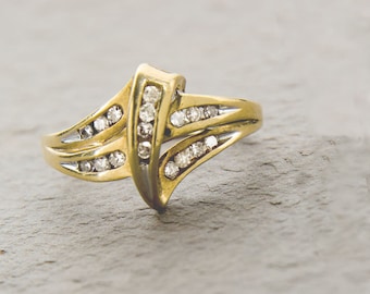 May include: A gold ring with a diamond-encrusted design. The ring has a unique, curved shape and features a row of diamonds on each side.