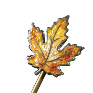 May include: A gold-toned pin with a detailed enamel maple leaf in shades of orange and yellow.