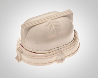May include: Ivory-colored, Art Deco style trinket box. The box features a rounded top with a leaf design and a layered, fan-like detail. The base is oval with a scalloped edge and additional leaf accents.