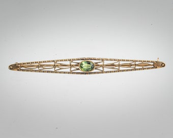 May include: A gold filigree brooch with a green gemstone in the center.