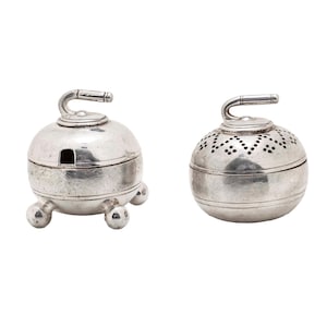 May include: Two silver-colored, spherical objects with curved handles. One rests on three ball feet and has a rectangular opening. The other has a perforated design. Both have a handle on top.
