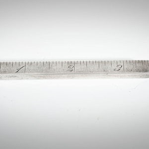 May include: A silver ruler with a loop at one end and a pointed tip at the other. The ruler is marked with numbers 1, 2, and 3.