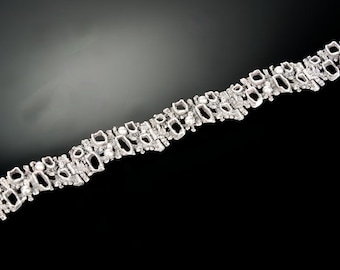 May include: A silver bracelet with a geometric design and white stones. The bracelet has a clasp closure.