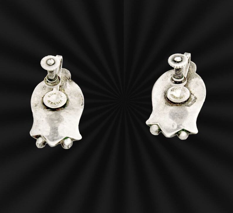 May include: A pair of silver tone clip-on earrings shaped like a flower with a screw back closure. The earrings are marked "SILVER" on the back.