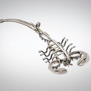 May include: A silver scorpion brooch with clear rhinestones. The brooch is detailed with a long, curved tail and a pin on the back.