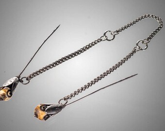 May include: A pair of silver chain and pin brooches with white and brown decorative beads. The pins are attached to a silver chain with two connecting rings.