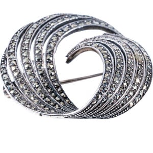 May include: A silver brooch with a swirling design set with marcasite stones.