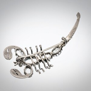 May include: A silver scorpion brooch with clear rhinestones. The brooch has a pin on the back for attaching to clothing.