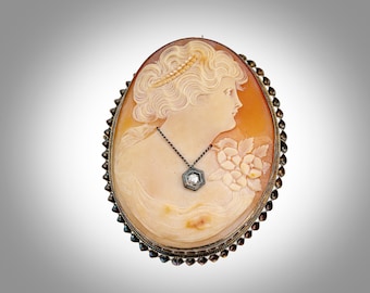 May include: A cameo brooch featuring a carved profile of a woman with a pearl crown and a pendant necklace with a diamond. The cameo is set in a silver frame with a beaded border.