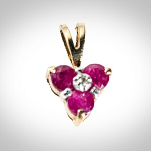 May include: A gold pendant with three ruby stones and a small diamond in the center.