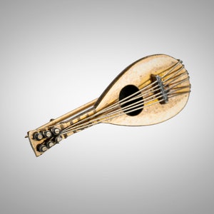 May include: A gold-toned metal brooch in the shape of a lute. The lute has a detailed design with strings and a sound hole.
