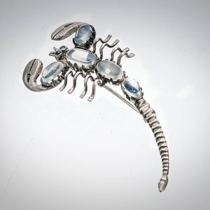 May include: A silver scorpion brooch with clear moonstone accents. The scorpion's tail is curled up and the brooch has a pin on the back.