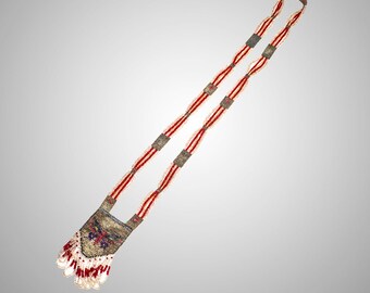 May include: A beaded shoulder bag with a long strap. The strap is red and white, with square metal accents. The bag itself is rectangular, with a floral design in the center and a white and red fringe at the bottom. The bag is made of small beads.