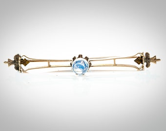 May include: A gold-toned brooch with a blue glass center stone and ornate floral accents on each end.