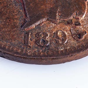 May include: Close-up of a copper coin with the year 1890 stamped on it. The coin is worn and has a brown patina.