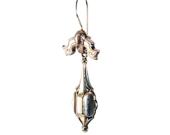 May include: A single, ornate silver earring with a decorative floral design. The earring features a long, teardrop-shaped pendant suspended from a curved hook. The design includes intricate details and a vintage aesthetic.