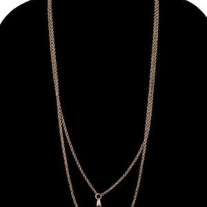 May include: A long, gold-colored chain necklace with a lobster clasp. The necklace is made of multiple strands of delicate chain, creating a layered effect. The background is solid black.