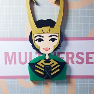May include: A stylized cutout of a character with a gold horned helmet, black hair, and a green cape. The character's face is detailed with a smile and dark eyes. The word "MULTIVERSE" is visible in the background.