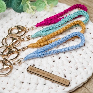 May include: Four crocheted keychains in blue, yellow, green, and pink colors with gold key rings and a wooden tag that says "@shanelle_kayla_crochet".