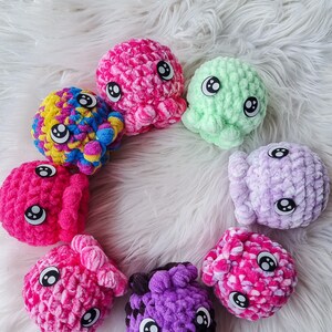 May include: A collection of eight crocheted octopus plushies in various colors, including pink, purple, green, yellow, and blue. Each octopus has black eyes and a textured, fluffy surface.