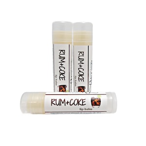 May include: Three clear tubes of lip balm with a brown label that reads "RUM+COKE lip balm". The label also features a cartoon image of a glass of rum and coke.