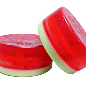 May include: Two round watermelon-scented soap bars. The bars are layered with red, white, and green, and have a speckled appearance.