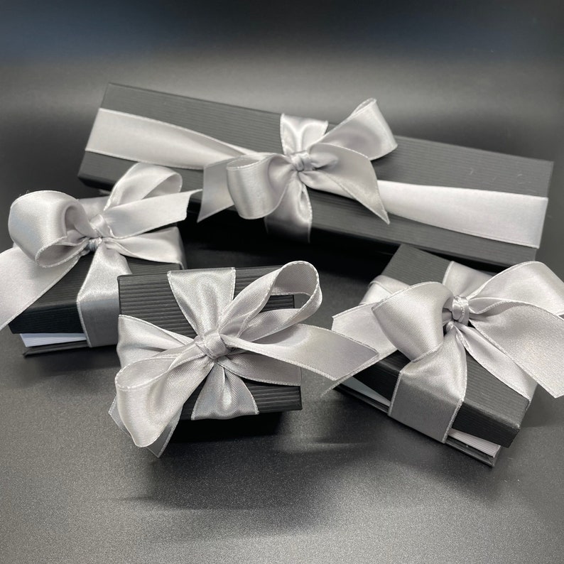 May include: Four black gift boxes with silver ribbon bows. The boxes are arranged in a semi-circle on a black surface.
