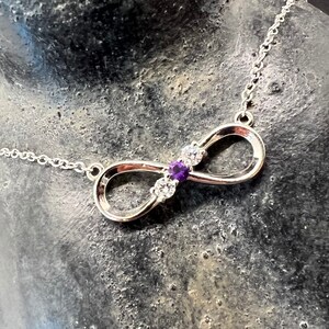 May include: A silver infinity necklace with a purple gemstone and clear cubic zirconia stones.