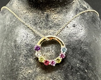 May include: A gold necklace with a circular pendant set with colorful gemstones. The pendant features a variety of small, round gemstones in shades of purple, pink, yellow, green, and blue.