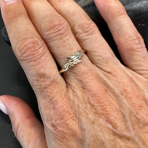 May include: A gold ring featuring a design of two hands clasped together. The ring is set with small blue gemstones.