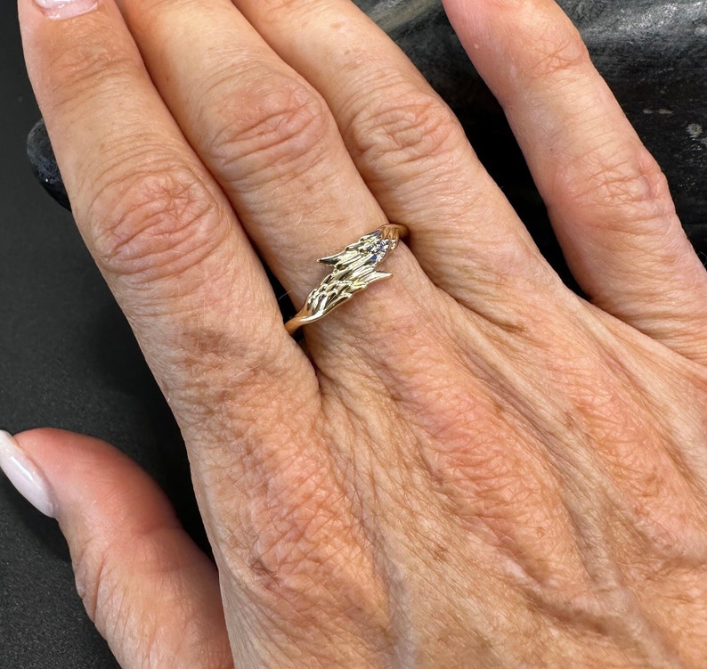 May include: A gold ring featuring a design of two hands clasped together. The ring is set with small blue gemstones.