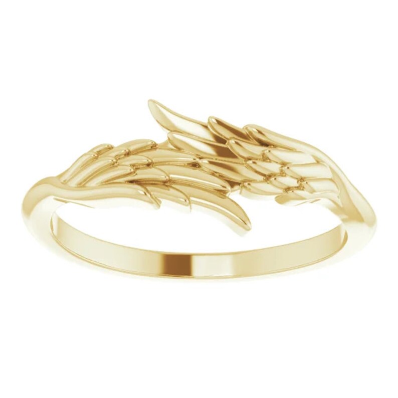 May include: A gold ring featuring a detailed angel wing design. The wings are spread out and curve around the band of the ring.