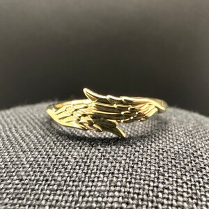 May include: A gold-coloured ring featuring a wing design. The ring is open and has a smooth, polished finish.