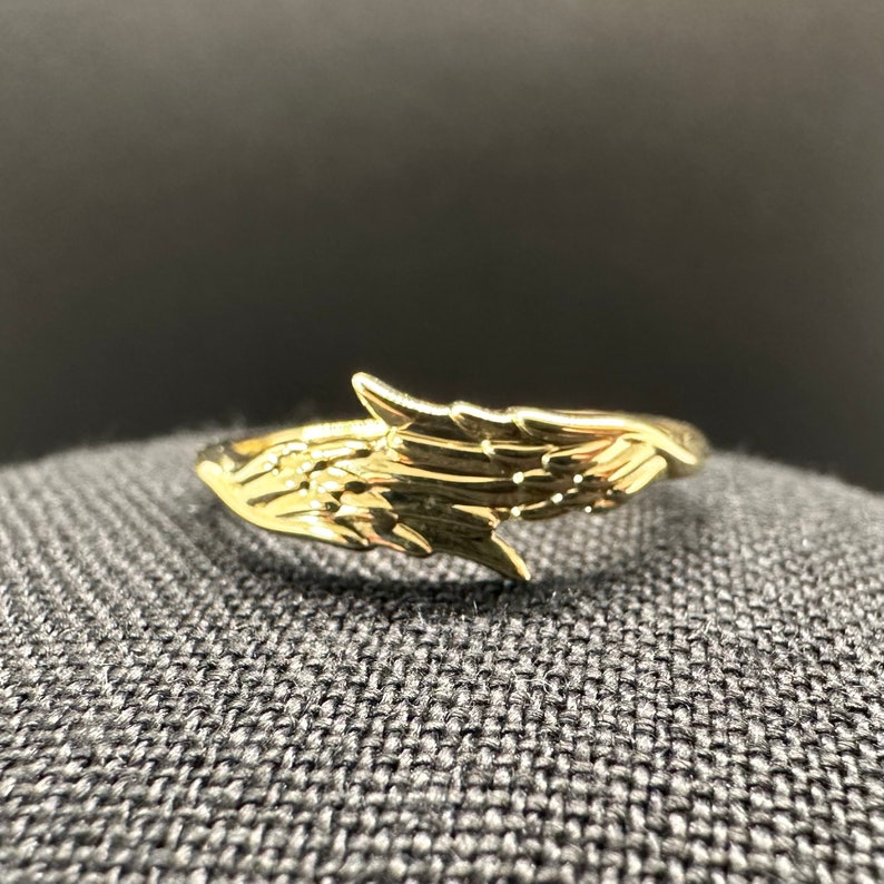May include: A gold-coloured ring featuring a wing design. The ring is open and has a smooth, polished finish.