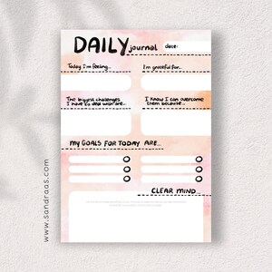 Op de afbeelding: Een dagelijkse journaalpagina met een aquarelachtergrond in roze en oranje tinten. De pagina bevat prompts voor zelfreflectie, zoals "Vandaag voel ik me..." en "Mijn doelen voor vandaag zijn..." Het journaal heeft ook de tekst "DAILY journal" bovenaan.