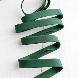 May include: A length of dark green bias tape, coiled and arranged on a white wooden surface. The tape is made of a soft fabric and is used for sewing and crafting projects. The tape is approximately 0.5 inches wide.