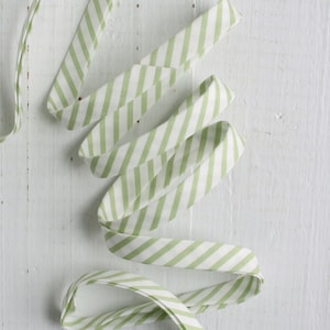 May include: A green and white striped ribbon is coiled on a white wooden surface.